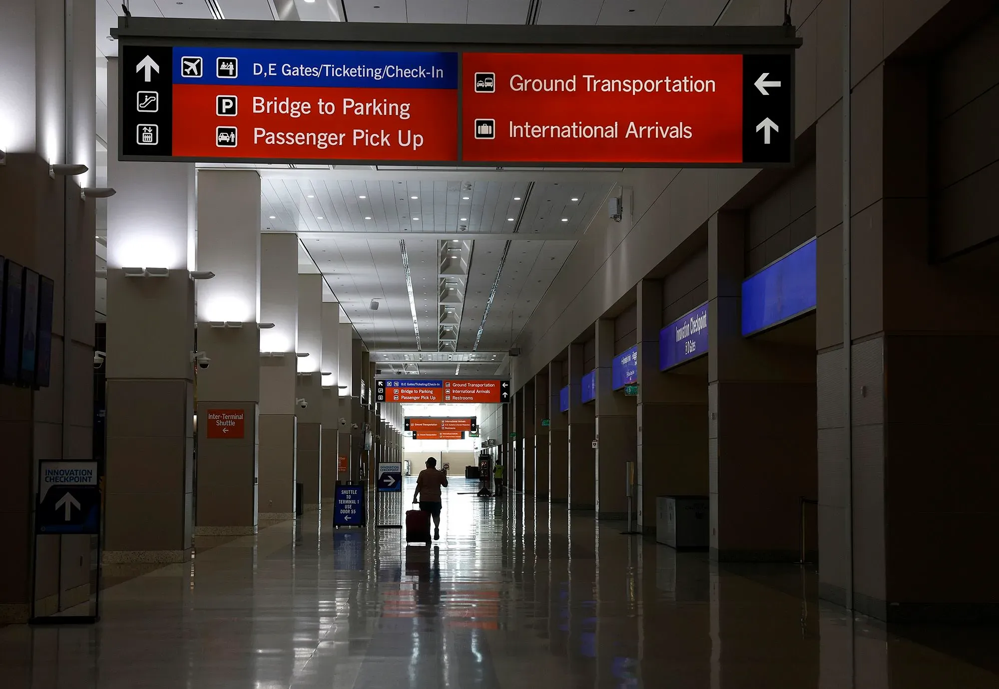 مطار هادئ مع لافتات توجيهية واضحة للركاب، تشير إلى مناطق مثل الوصول الدولي والنقل الأرضي، مما يعكس تأثير انخفاض السياحة الكندية.