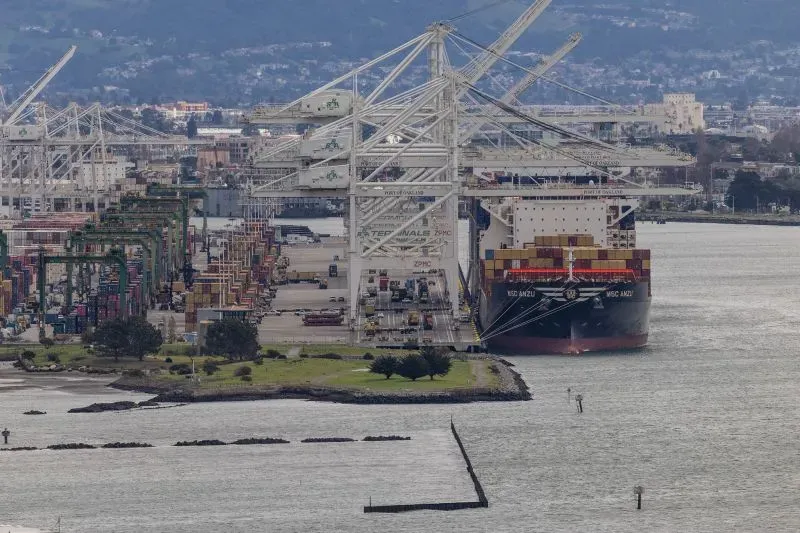 صورة لميناء مزدحم يظهر سفينة حاويات كبيرة راسية، مع العديد من الرافعات والشاحنات، تعكس تأثير التعريفات الجمركية على التجارة.