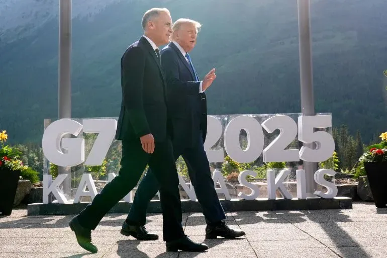 ترامب وكارني يسيران معًا أمام لافتة قمة مجموعة السبع 2025 في كندا، وسط مناظر جبلية خلابة، في سياق التوترات التجارية الجديدة.