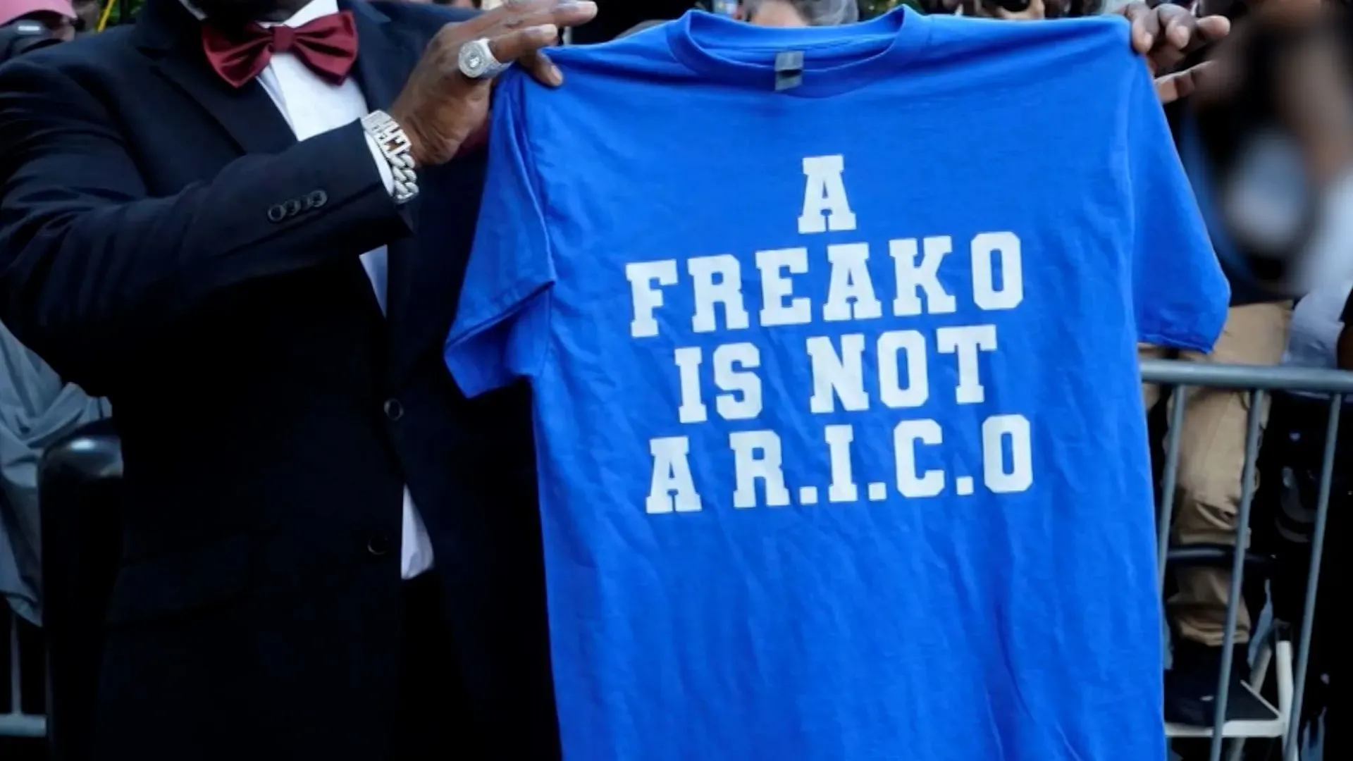 قميص أزرق يحمل عبارة "A FREAKO IS NOT A R.I.C.O" يرفعه أحد المؤيدين خارج المحكمة، في إشارة إلى قضية شون كومبس.