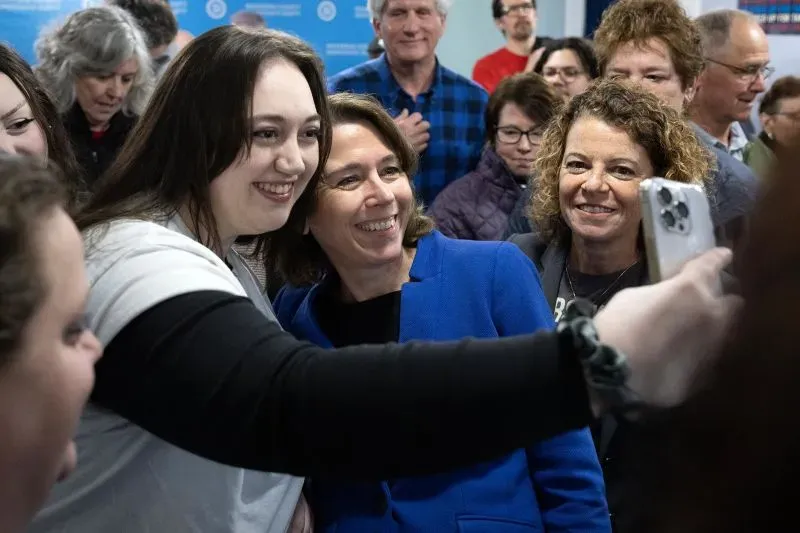 سيدة تبتسم وتلتقط سيلفي مع مجموعة من الأشخاص في تجمع انتخابي، مما يعكس حماس الحملة الانتخابية في ويسكونسن.