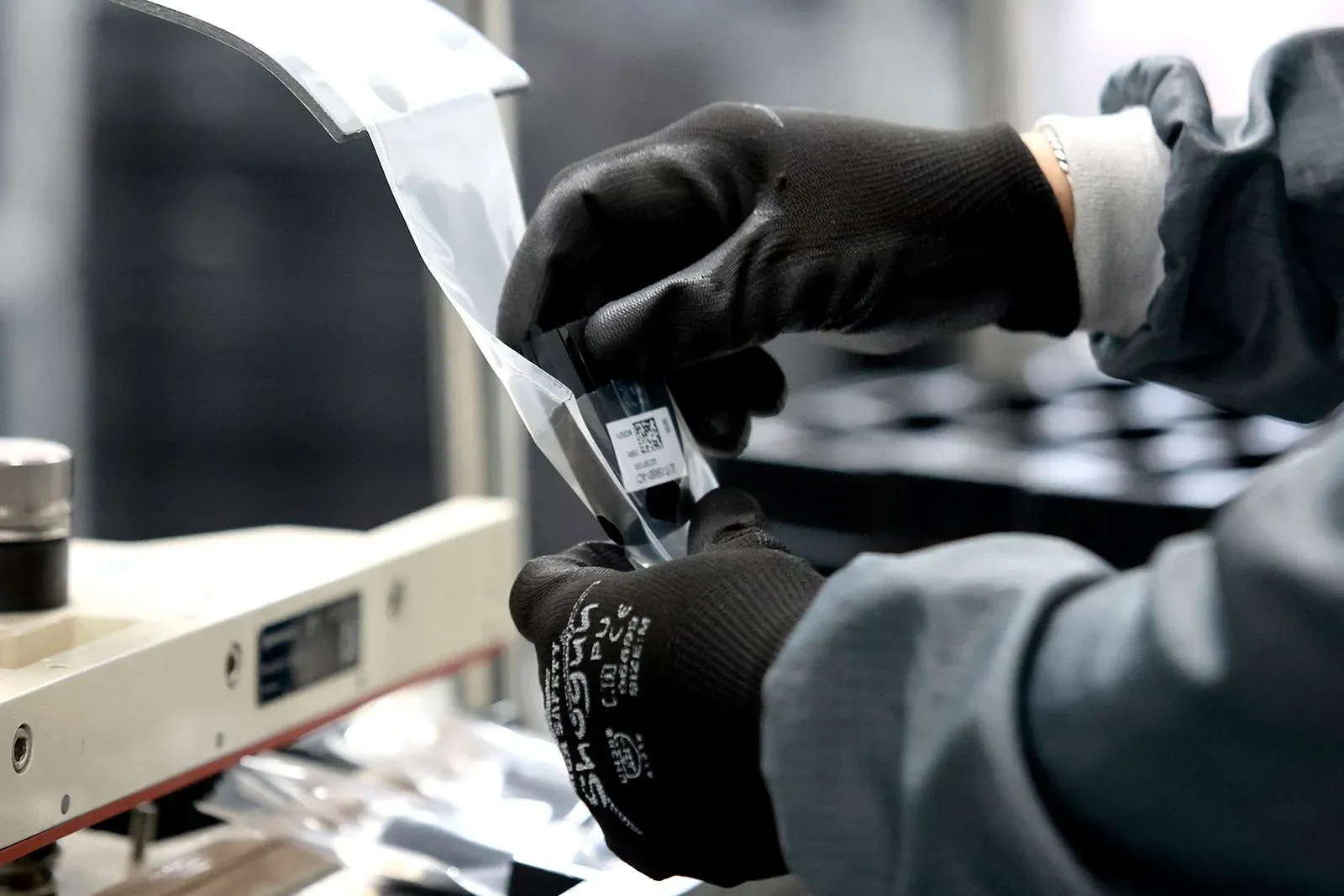 عامل يرتدي قفازات يقوم بمعالجة مكونات إلكترونية في مصنع، مما يعكس تأثير التعريفات الجمركية على صناعة السيارات والإلكترونيات.