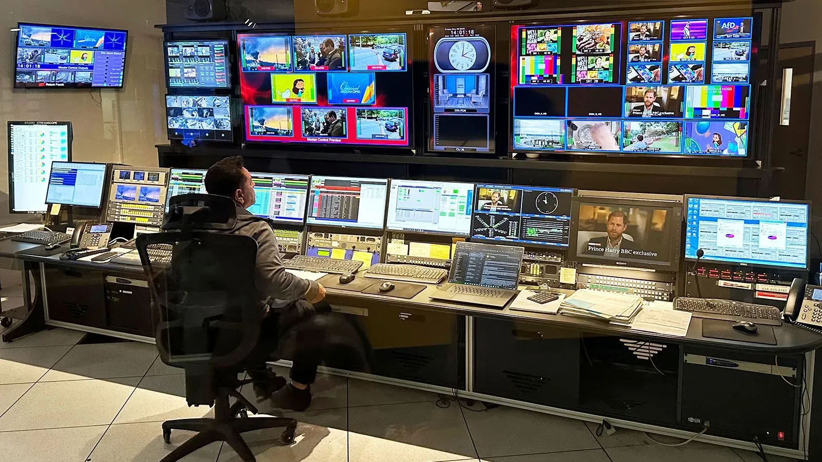 غرفة التحكم في البث، حيث يتواجد مشغل أمام عدة شاشات تعرض محتوى مختلف، تعكس التحديات التي تواجه وسائل الإعلام العامة.