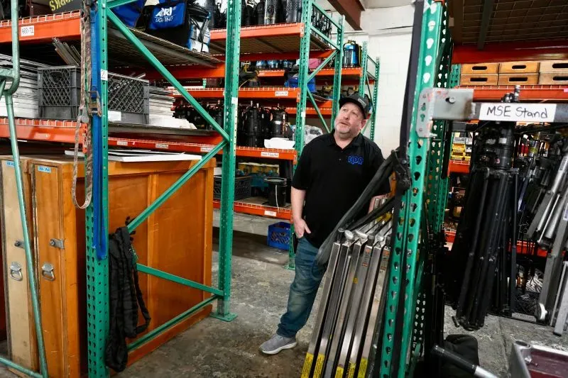 رجل يقف في مستودع لتأجير معدات التصوير، محاطًا بأرفف مليئة بالأدوات والمعدات، يعكس تأثير تباطؤ الإنتاج في هوليوود.