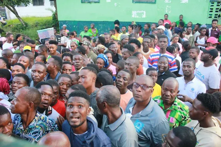 حشد كبير من الناس في ليبيريا، يعبرون عن حماسهم خلال حدث اجتماعي، مع وجود مبانٍ خضراء في الخلفية.