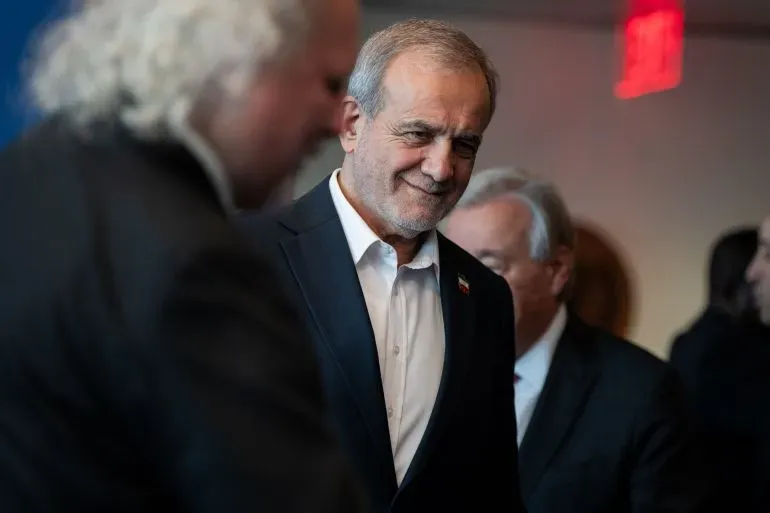 الرئيس الإيراني مسعود بيزشكيان مبتسم خلال حدث، مع التركيز على قضايا الحرب الأمريكية الإسرائيلية وتأثيرها على إيران.