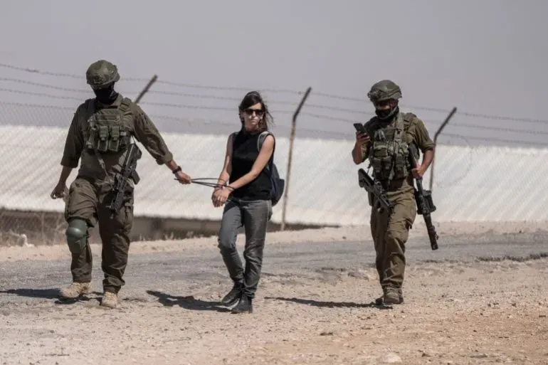 اعتقال ناشطة فلسطينية من قبل جنود إسرائيليين في الضفة الغربية، مع سياج خلفي، يعكس التوترات المستمرة في المنطقة.