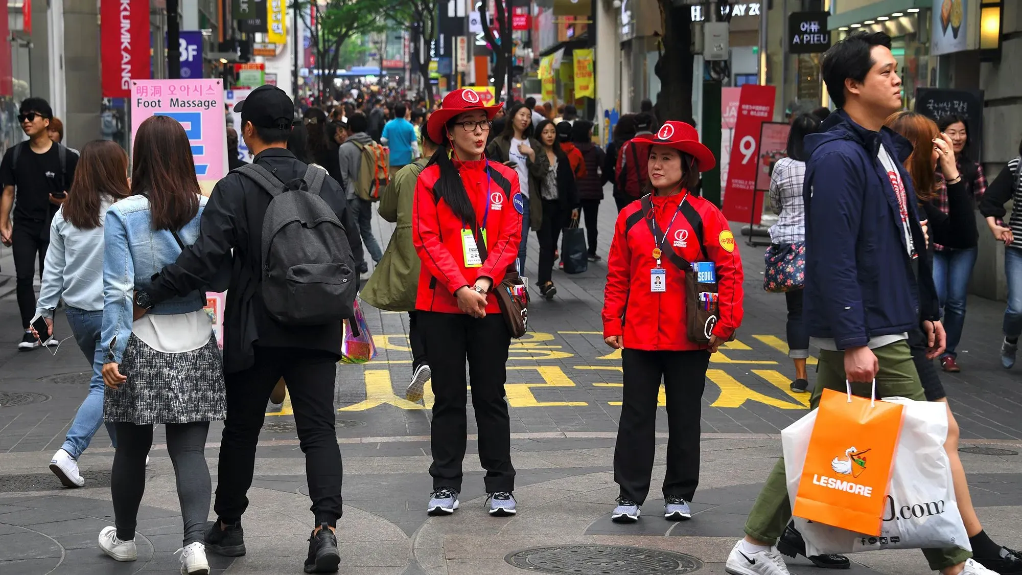 موظفان في مركز معلومات سياحي يرتديان قمصانًا حمراء وقبعات رعاة البقر، يقفان في منطقة مزدحمة في سيول، كوريا الجنوبية.