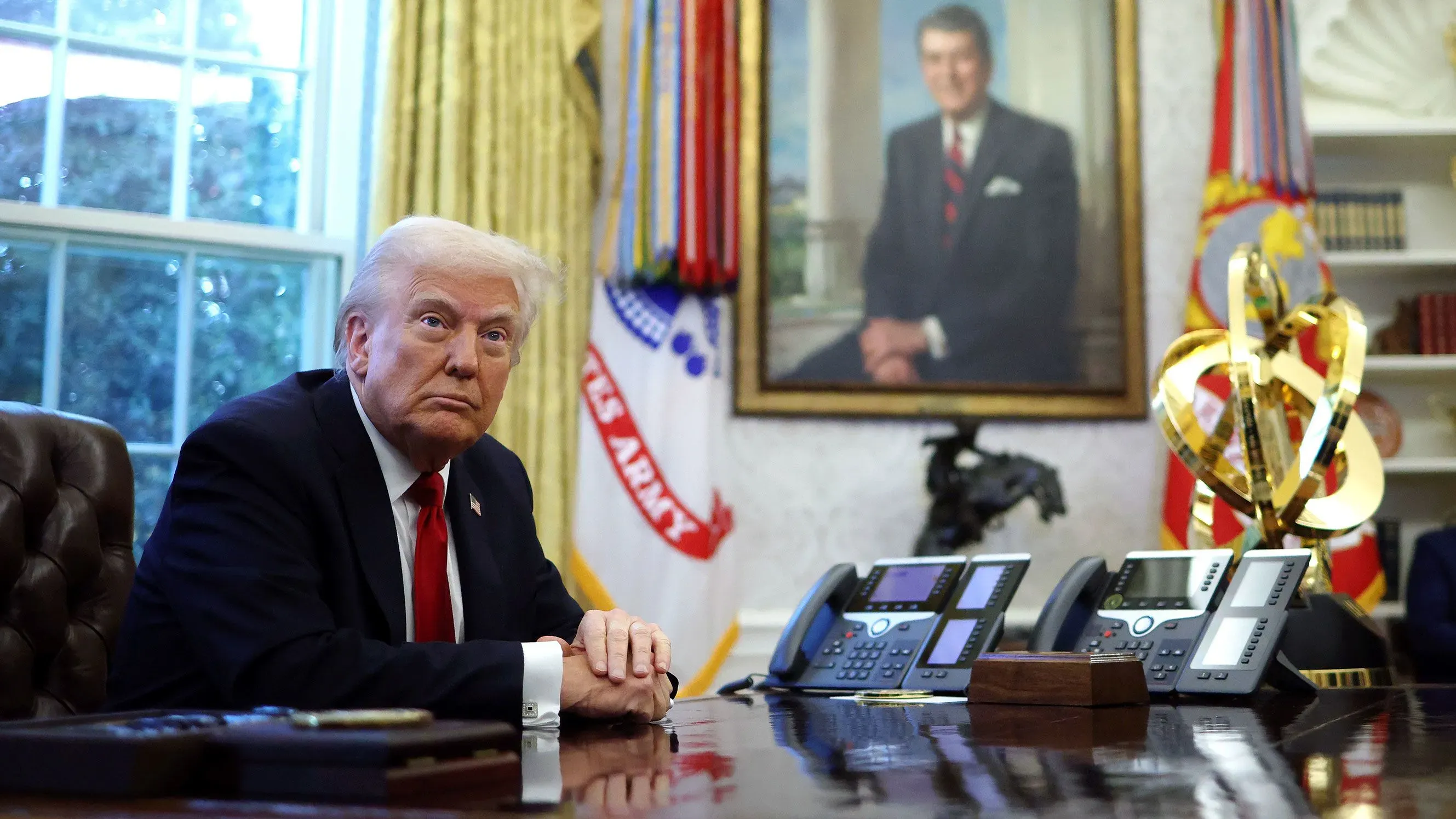 ترامب يجلس في المكتب البيضاوي، مع وجود لوحة خلفه، محاطًا بأجهزة الهاتف. تعكس تعابيره قلقًا بشأن تأثير التعريفات الجمركية.