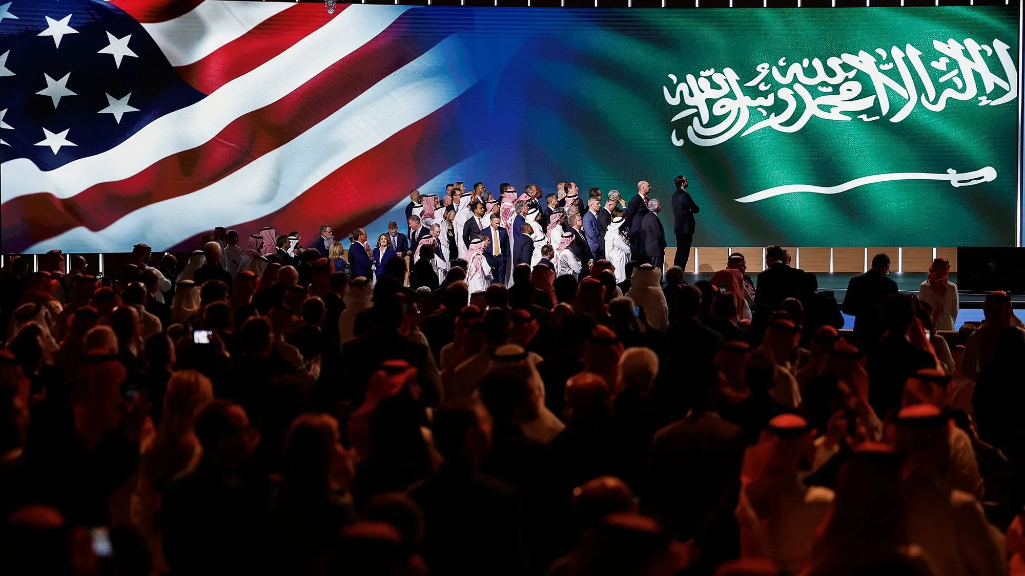 اجتماع بين مسؤولين أمريكيين وسعوديين في حدث بارز، مع خلفية تحمل العلم الأمريكي والعلم السعودي، يعكس التعاون في مجال الذكاء الاصطناعي.