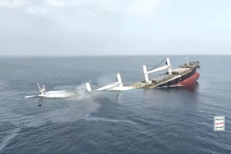 سفينة غارقة في البحر الأحمر، تُظهر آثار الهجوم الحوثي، مع وجود دخان يتصاعد من جانبها، تعكس تصاعد التوترات في المنطقة.