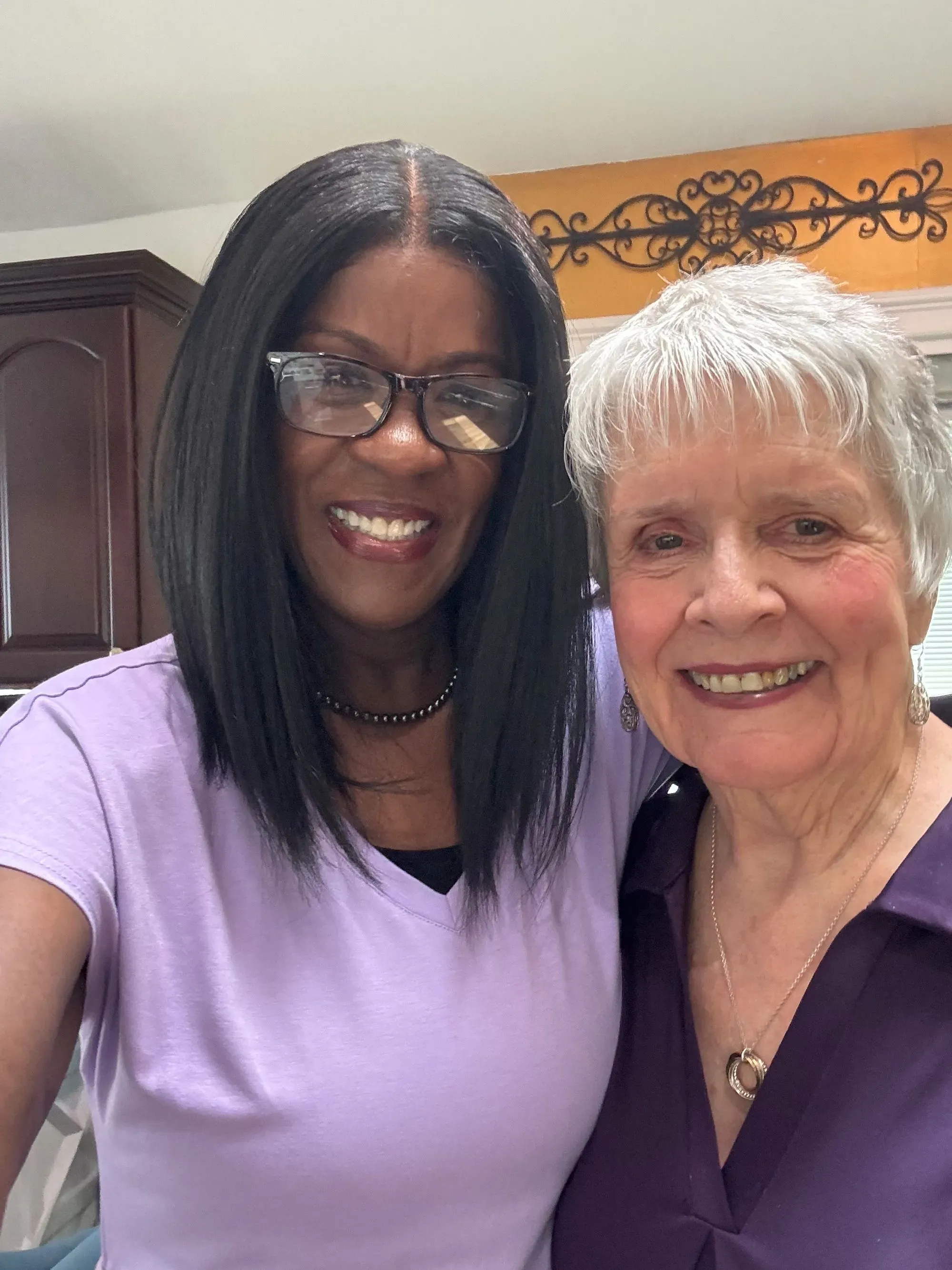 صورة تظهر امرأتين مبتسمتين، إحداهما ذات شعر أسود طويل والأخرى بشعر رمادي قصير، تعكسان دعمًا عاطفيًا خلال رحلة تحسين الصحة العقلية.