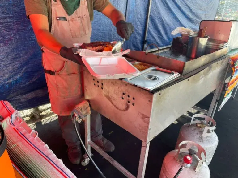 بايو يقوم بتقديم أطباق من الدجاج والكارني أسادا في كشك طعام في شرق هوليوود، وسط أجواء من التوتر والخوف بين المهاجرين.