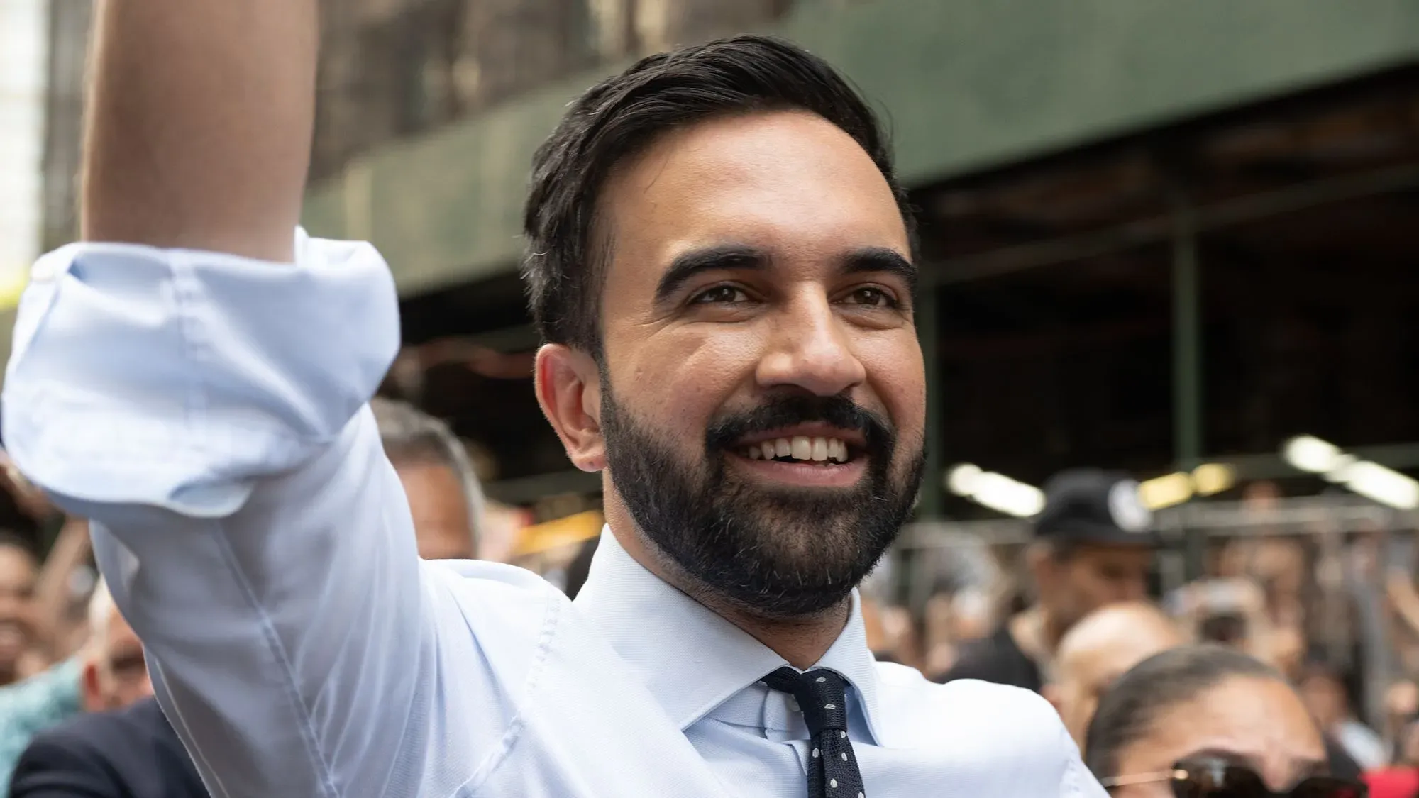 زهران ممداني، المرشح لمنصب عمدة نيويورك، يبتسم ويرفع يده خلال حملة انتخابية، مع التركيز على قضايا الإسكان الميسور.